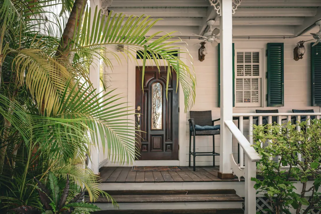 Welcoming white clapboard house front with a dark wood door and a porch chair in soft daylight