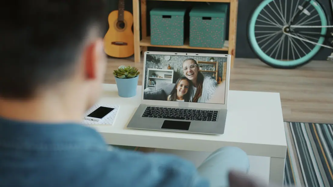 A man at home video-calls a smiling woman and girl on his laptop
